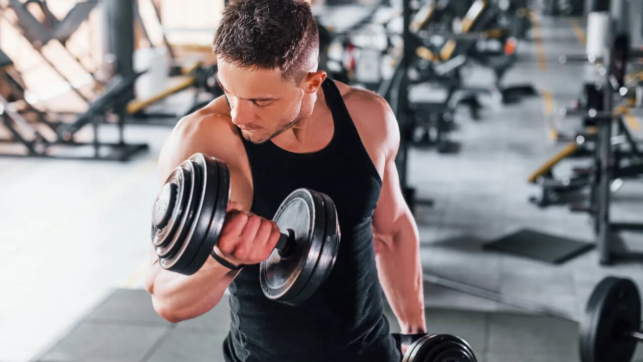 Liting dumbbells. Young sportive strong man in black wear have workout day in gym.; Shutterstock ID 1779955331