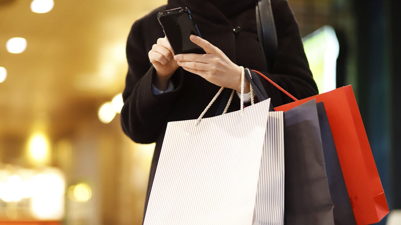 Woman Using Mobile Phone While Holding Shopping Bags; Shutterstock ID 1800649339