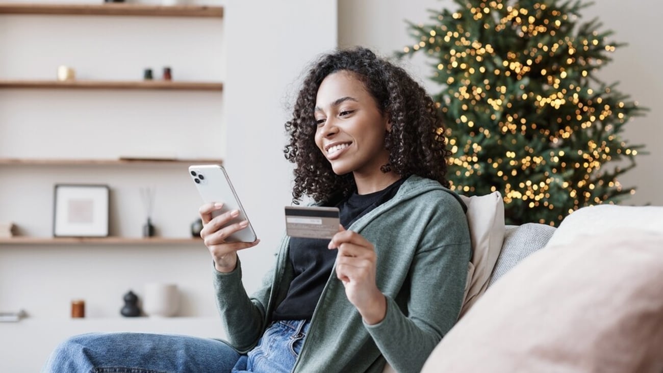 Shopping online during holidays. Woman using smartphone and credit card, ordering Christmas gifts. Online shopping, e-commerce, internet banking, spending money concept; Shutterstock ID 2220883709