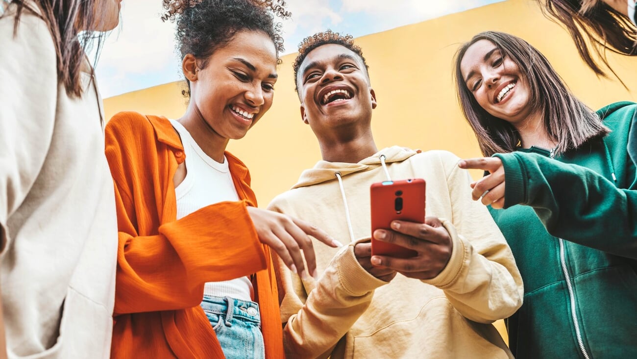 Diverse young people using smart mobile phone device outdoors - Multiracial friends watching smartphone together - Teenagers uploading reel video on social media platform - Youth culture concept; Shutterstock ID 2275871901