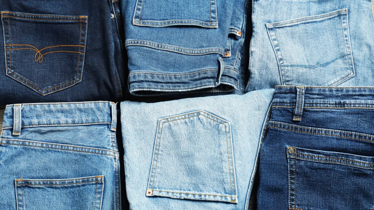 Different stylish jeans as background, top view; Shutterstock ID 2608221783