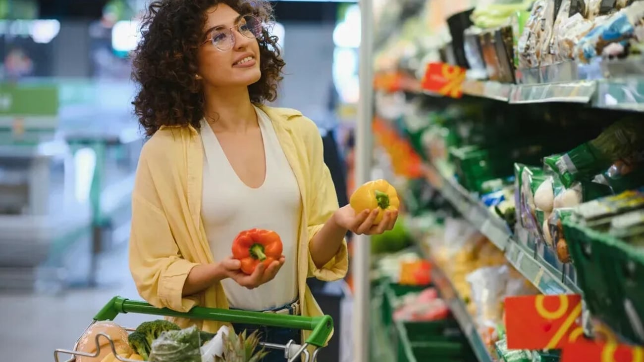 Customer comparing vibrant yellow and red bell peppers while shopping in a supermarket aisle, thoughtfully selecting fresh produce for a healthy meal; Shutterstock ID 2633120847
