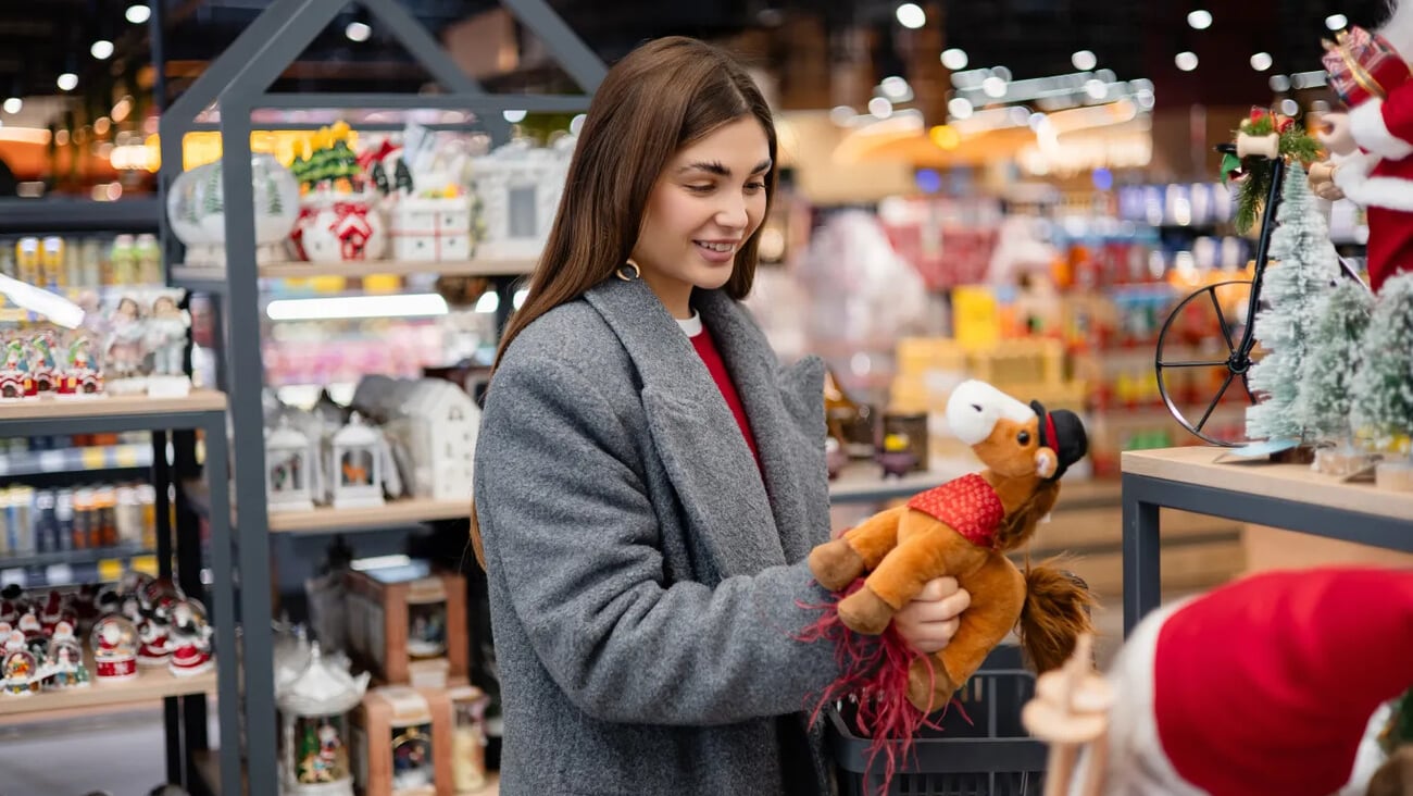 Woman choosing a toy horse decoration in a holiday store. Symbol of the 2026 Year of the Horse, seasonal shopping and festive preparations.; Shutterstock ID 2706897233