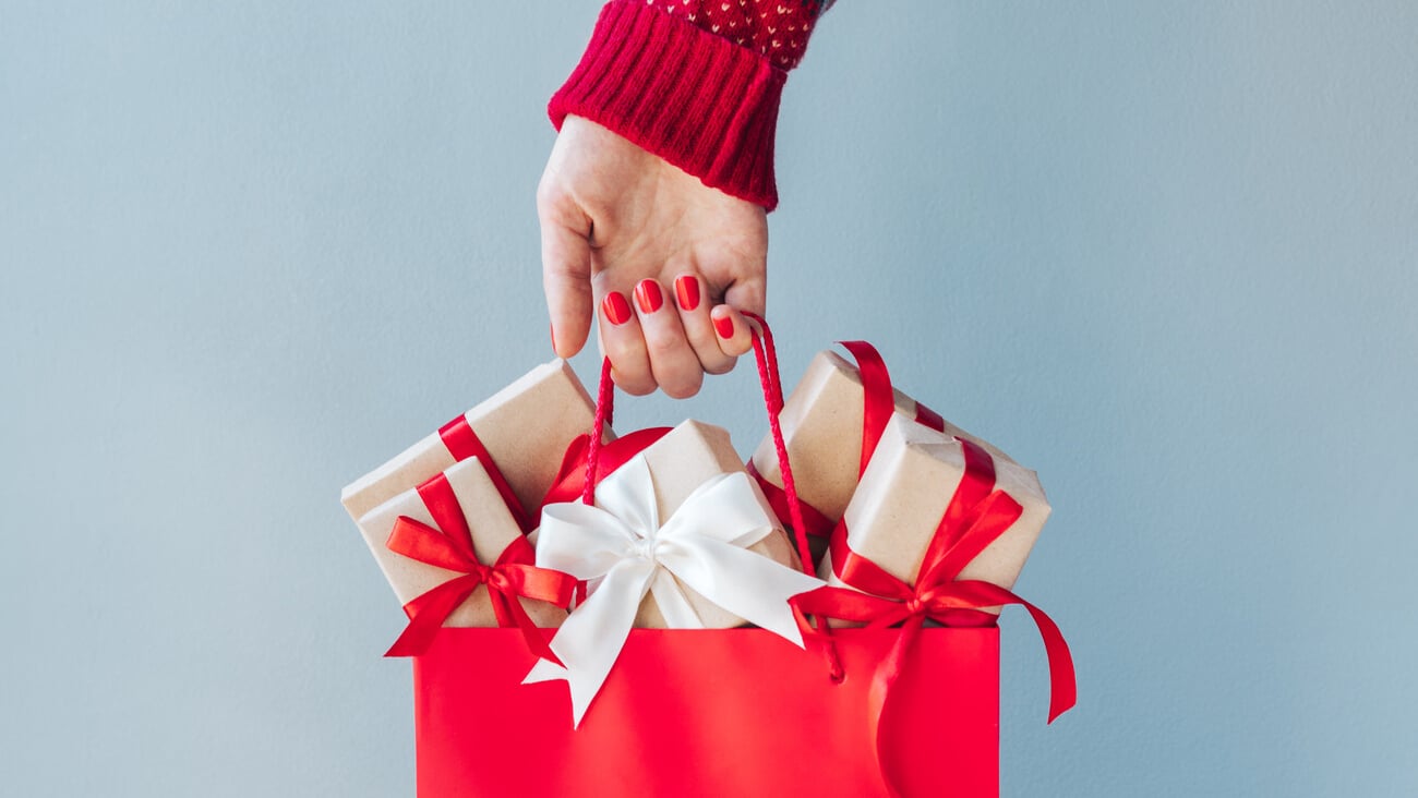 Cropped image of female hand with red polished nails holding shopping bag full of christmas gift boxes. Holiday sale concept. ; Shutterstock ID 1816229015