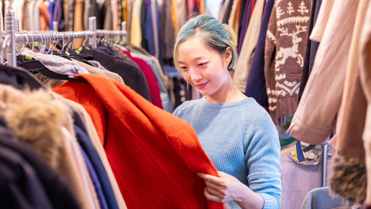 Stylish Asian woman is choosing second hand sweater from the clothing shop for winter season fashion to keep warm at the new year and christmas holiday; Shutterstock ID 2326173193