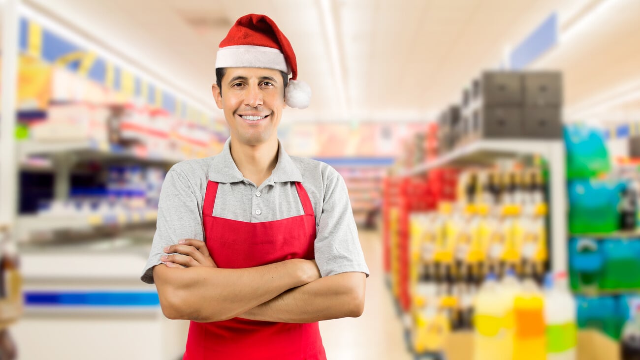 portrait of shopman at the supermarket with crossing arms wearing santa hat; Shutterstock ID 495589945