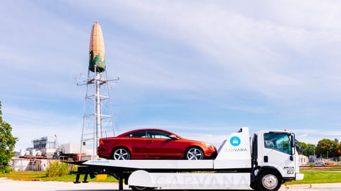 car on flatbed passing giant corn ear