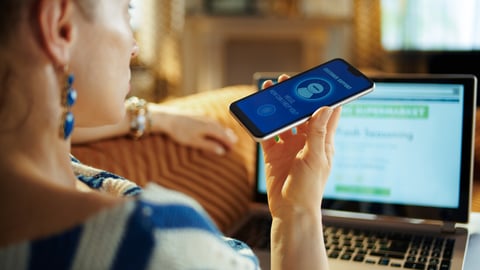 Over shoulder shot of young woman laying on sofa at modern home in sunnny hot summer day getting help from voice robot support while order food digital at online supermarket.; Shutterstock ID 1444176149