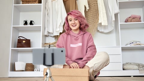 Happy hipster gen z teen girl fashion social media channel blogger with pink hair wear hoodie recording unboxing vlog on phone video camera tutorial sit on floor with online store clothes order box.; Shutterstock ID 1736626433
