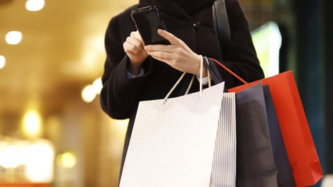 Woman Using Mobile Phone While Holding Shopping Bags; Shutterstock ID 1800649339