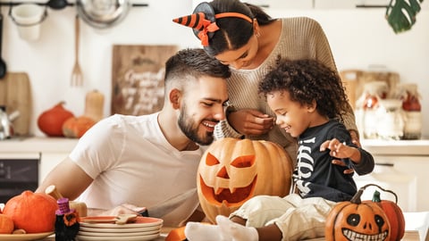 Cheerful multi ethnic family parents with son smiling  while creating jack o lantern from pumpkin during Halloween celebration in kitchen at home.; Shutterstock ID 1833746497