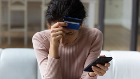 Upset latina female internet shopper sit on couch hold phone with opened web shop ebank page suffer of overspending money from card account. Frustrated young lady lost savings as scam operation result; Shutterstock ID 1954985212
