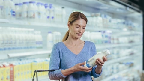 woman chooses dairy products holding a bottle of milk in her hands. female stands in a grocery store picking with a shopping basket. Studies and reads information on the label Considers makes choices; Shutterstock ID 2201735577