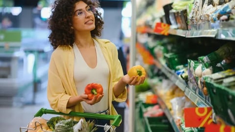 Customer comparing vibrant yellow and red bell peppers while shopping in a supermarket aisle, thoughtfully selecting fresh produce for a healthy meal; Shutterstock ID 2633120847