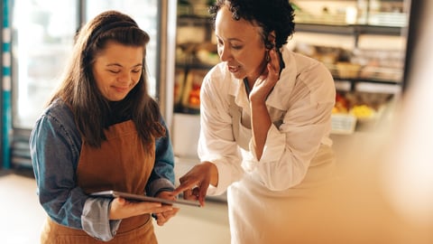 Two supermarket workers managing online grocery orders on a digital tablet. Empowered woman with Down syndrome running a successful small business with her female colleague.; Shutterstock ID 2174124369