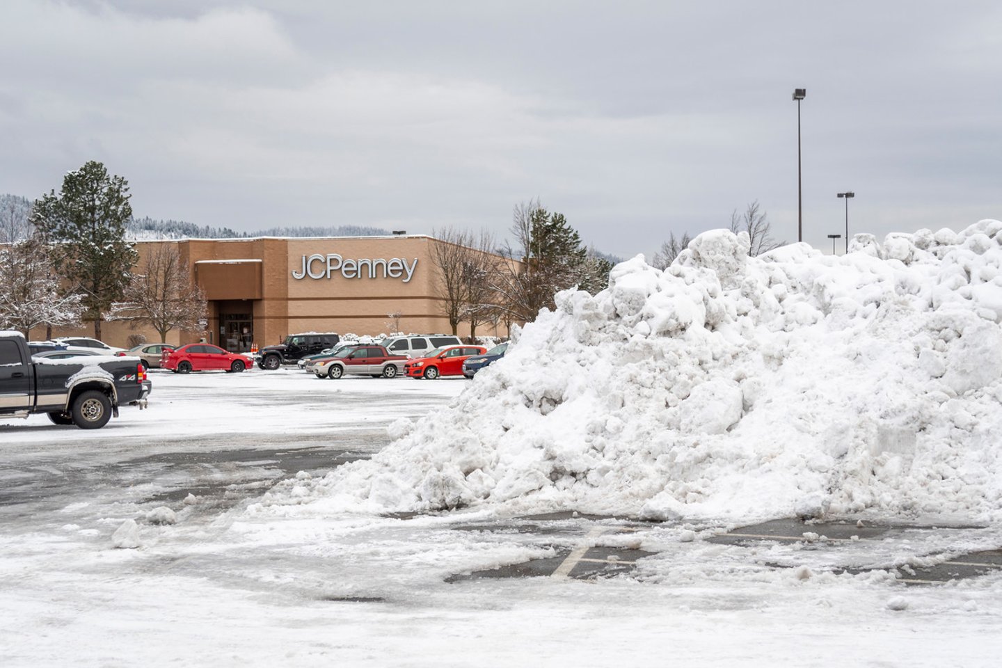 Coeur d'Alene, Idaho USA - January 14 2019: A massive pile of plowed snow after a winter storm sits in a parking lot of a shopping mall with a department store in view behind.; Shutterstock ID 1616576776