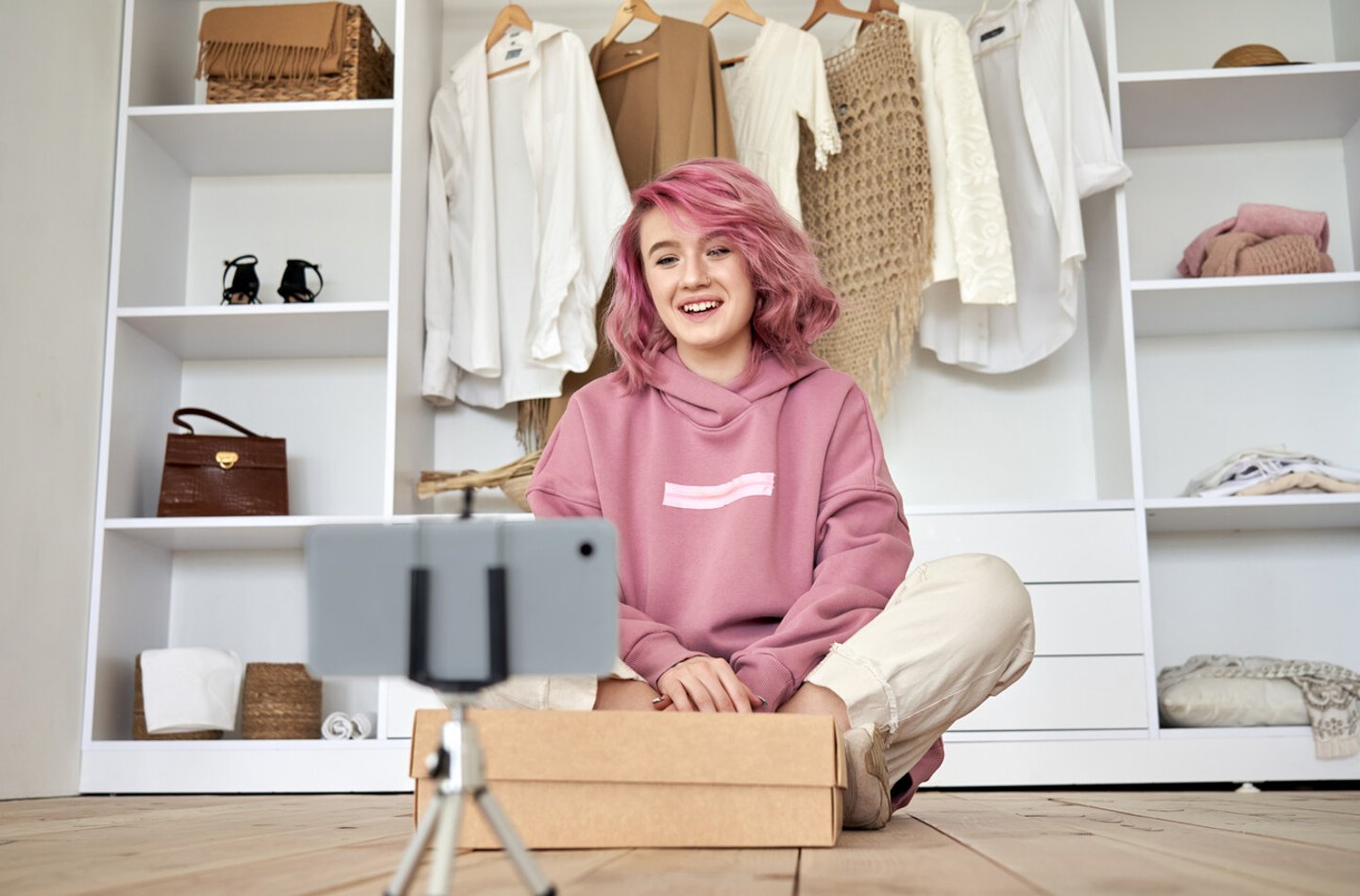 Happy hipster gen z teen girl fashion social media channel blogger with pink hair wear hoodie recording unboxing vlog on phone video camera tutorial sit on floor with online store clothes order box.; Shutterstock ID 1736626433