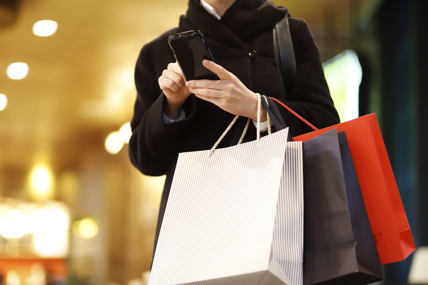 Woman Using Mobile Phone While Holding Shopping Bags; Shutterstock ID 1800649339