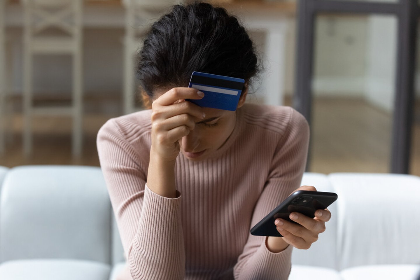 Upset latina female internet shopper sit on couch hold phone with opened web shop ebank page suffer of overspending money from card account. Frustrated young lady lost savings as scam operation result; Shutterstock ID 1954985212
