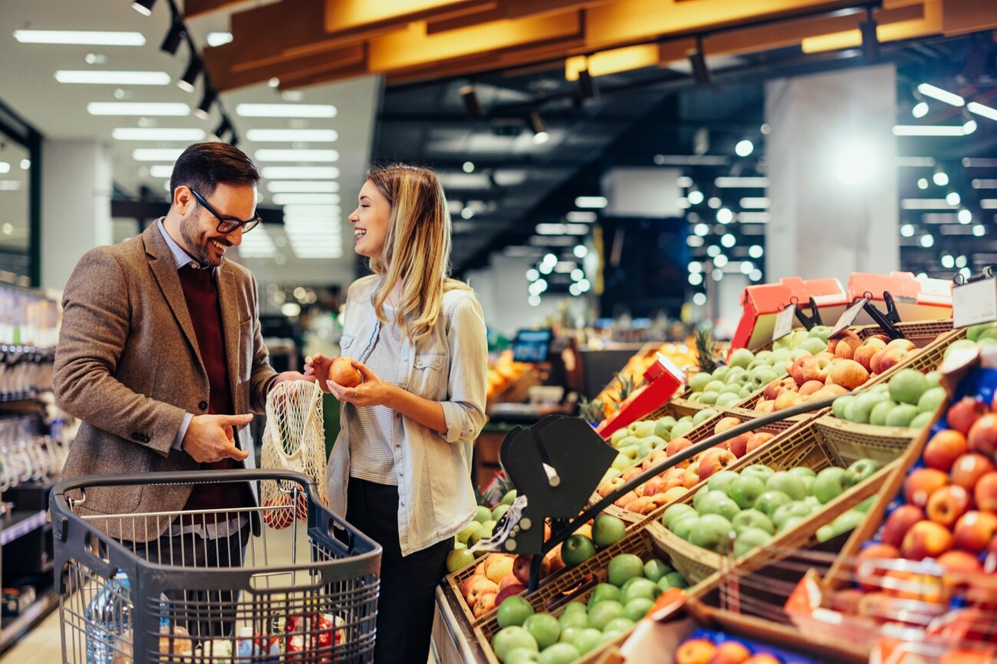 Cheerful couple choosing fruit at groceries department of the supermarket. Man holding mesh bag and woman holding fruits. Shopping at the modern mall; Shutterstock ID 2159860109