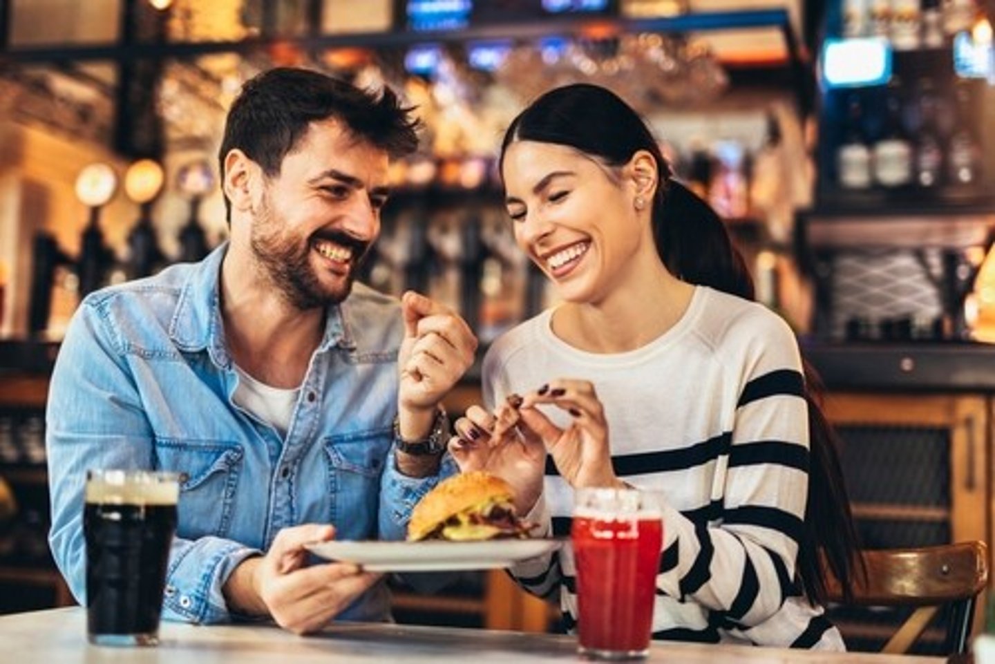 Young couple in love having fun spending leisure time together at restaurant, eating burgers and drinking beer; Shutterstock ID 2240724321