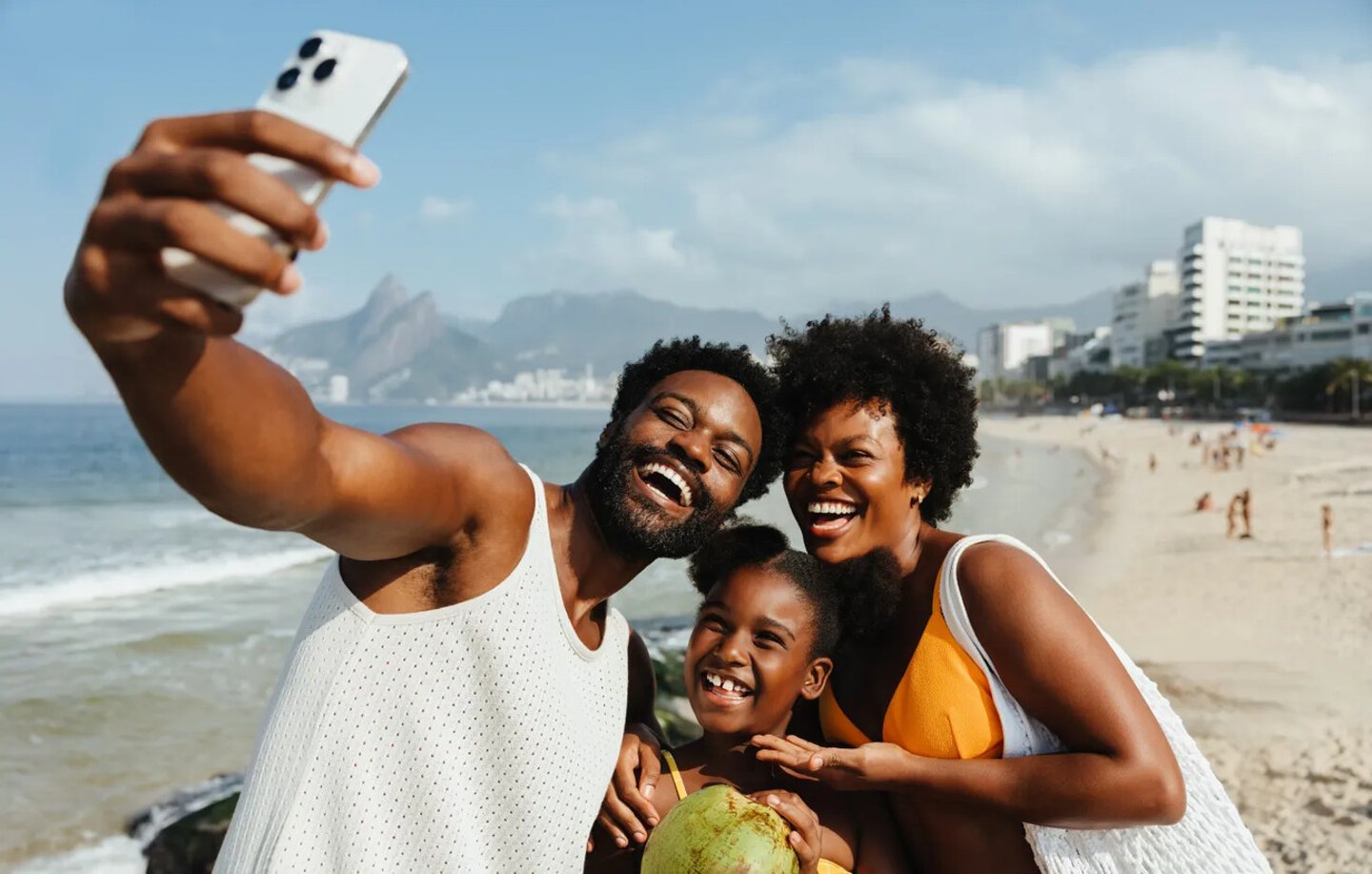 A cheerful Brazilian family enjoys a sunny day at a beach in Rio de Janeiro, capturing the moment with a selfie. The scene showcases joy and togetherness, with the iconic cityscape in the background.; Shutterstock ID 2545766889