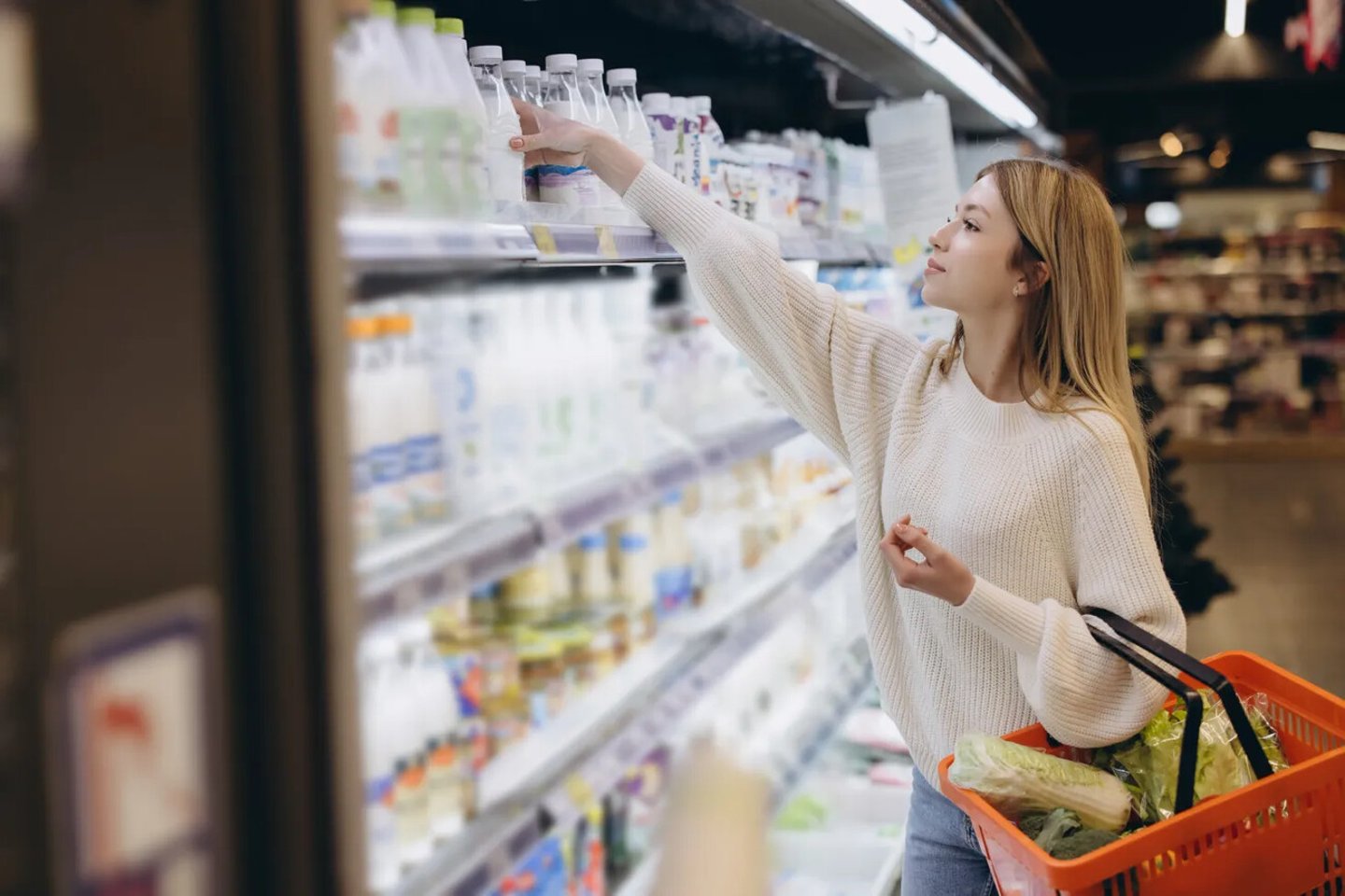 Young woman shopping for groceries, reaching for bottled water in refrigerated aisle of supermarket; Shutterstock ID 2558906661