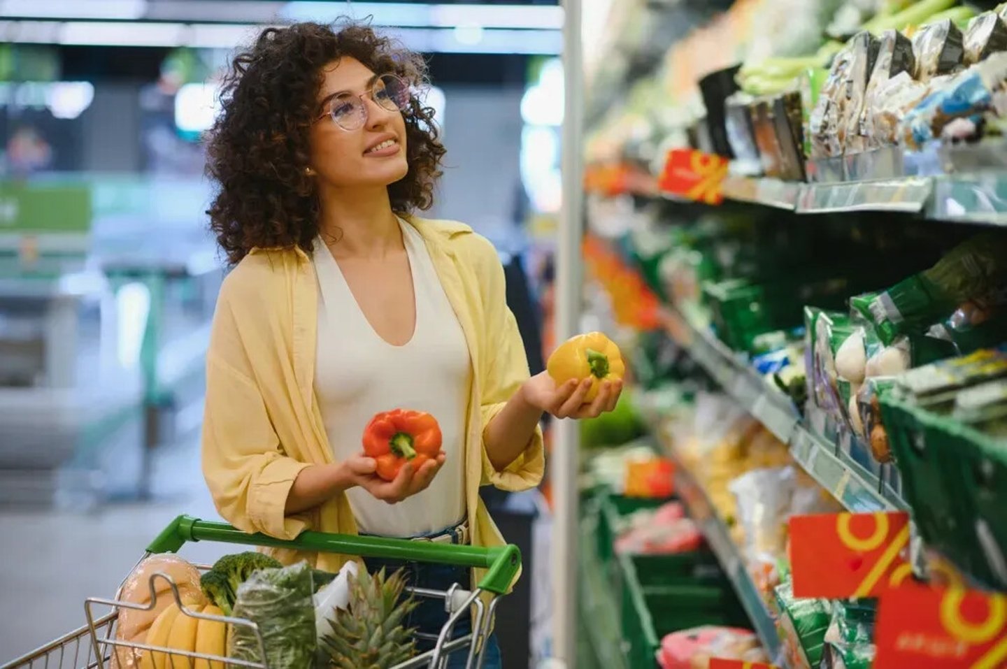 Customer comparing vibrant yellow and red bell peppers while shopping in a supermarket aisle, thoughtfully selecting fresh produce for a healthy meal; Shutterstock ID 2633120847