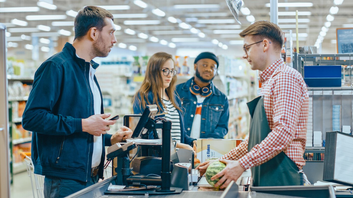 At the Supermarket: Checkout Counter Customer Pays with Smartphone for His Items. Big Shopping Mall with Friendly Cashier, Small Lines and Modern Wireless Paying Terminal System.; Shutterstock ID 1275256225