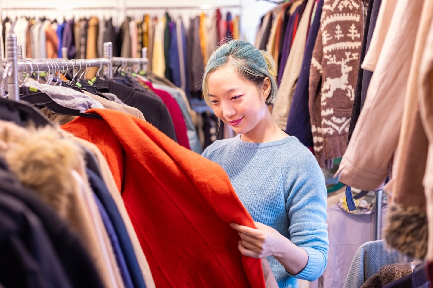 Stylish Asian woman is choosing second hand sweater from the clothing shop for winter season fashion to keep warm at the new year and christmas holiday; Shutterstock ID 2326173193