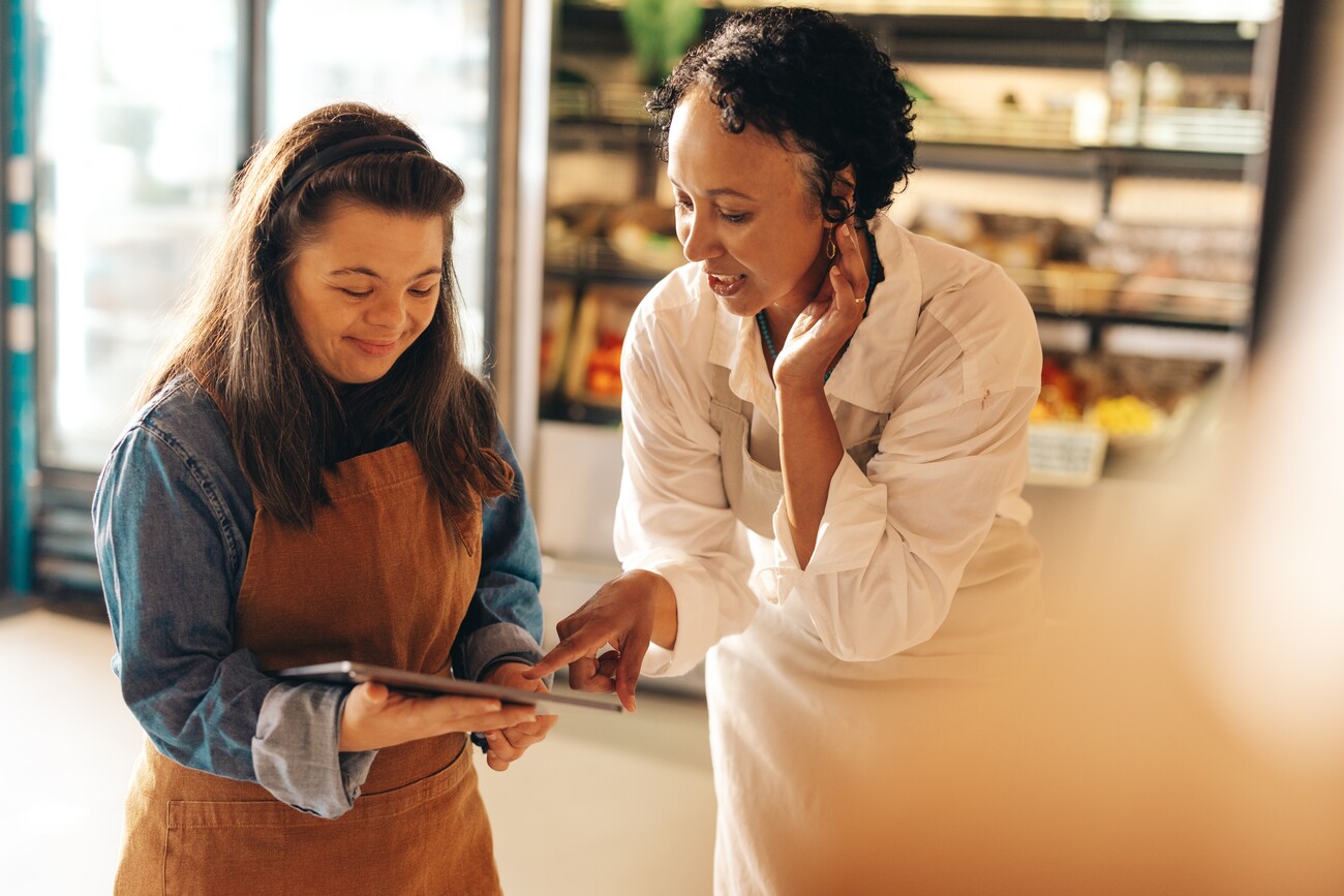 Two supermarket workers managing online grocery orders on a digital tablet. Empowered woman with Down syndrome running a successful small business with her female colleague.; Shutterstock ID 2174124369