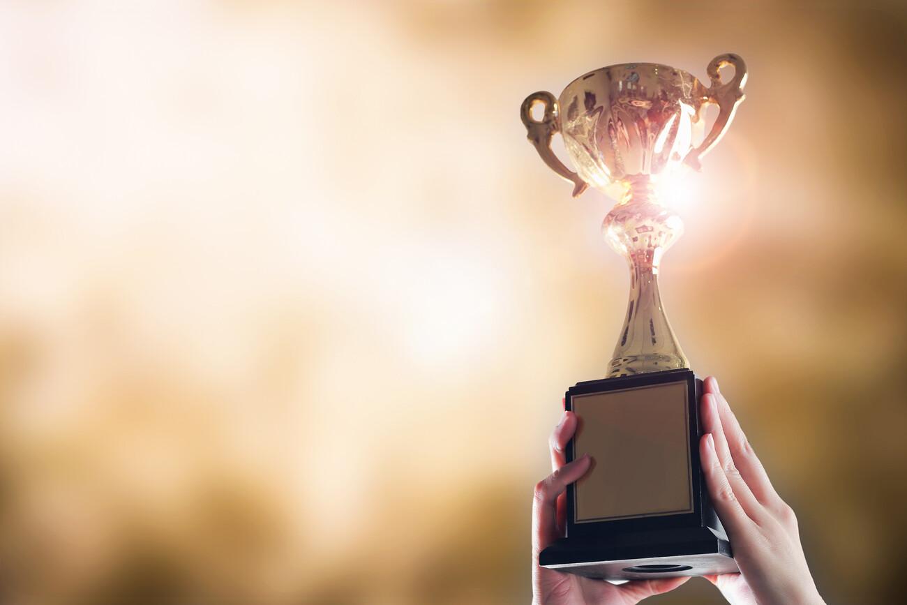 Hands holding trophy cup on gold blurry bokeh background.; Shutterstock ID 1034397511