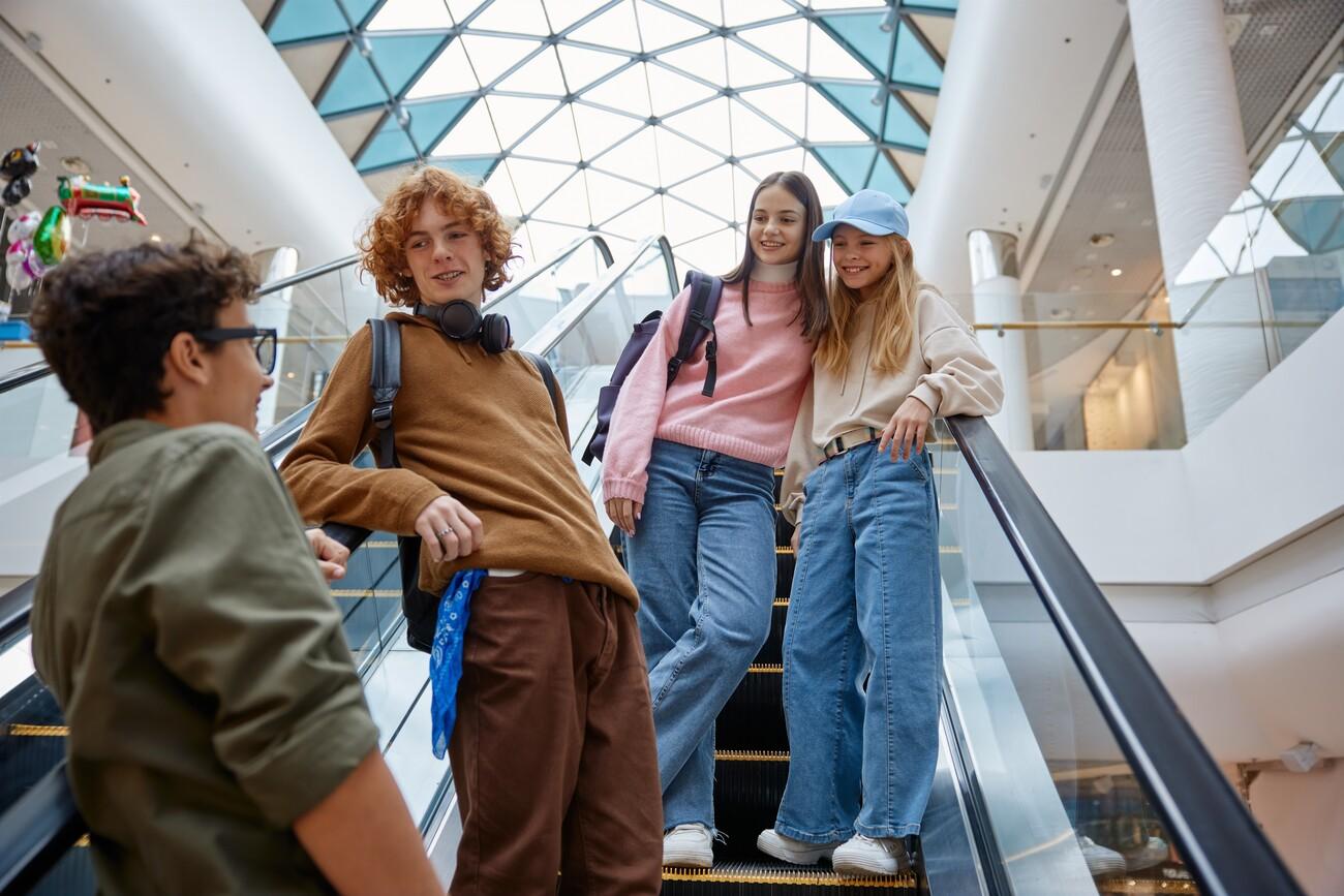 Happy teenage friends team moving staircase at shopping mall; Shutterstock ID 2407962477